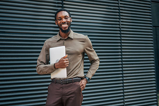 istock Smiling businessman holding laptop standing by modern office building 2235357027
