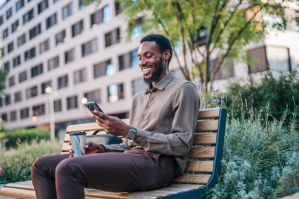 istock Smiling businessman using smartphone and drinking coffee on a bench 2235357555