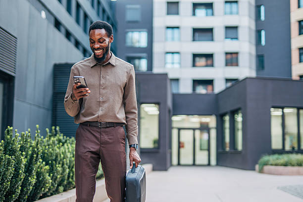 istock Smiling businessman walking and using smartphone in urban setting 2235358366