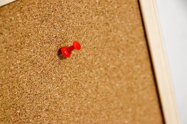 A close-up shot of a bright red pushpin fixed on a corkboard surface. This image highlights the vivid color contrast and texture, making it ideal for organizational themes.