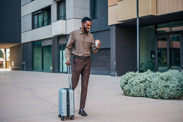 istock Businessman walking with suitcase and coffee outside modern building 2235358991