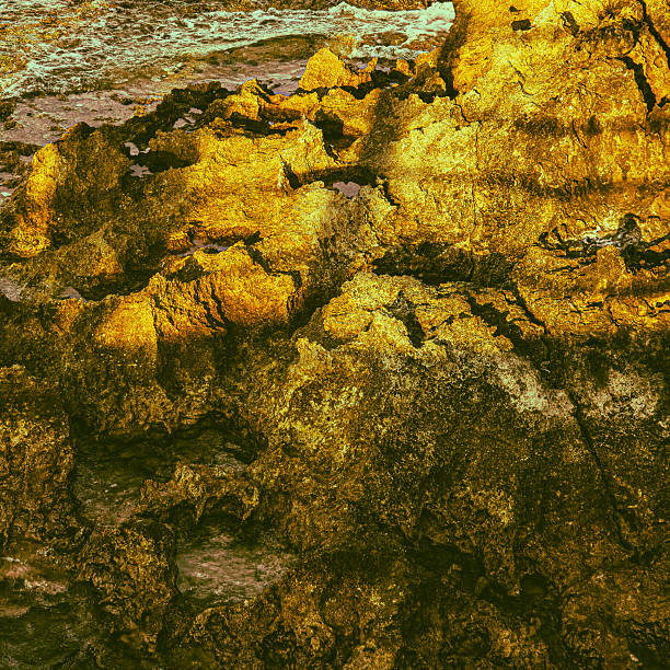 Close-up of golden rocky coastal surface with abstract light and shadow pattern on the Mediterranean coast of Cyprus. Textured natural background with artistic mineral-like effect, ideal for design and creative concepts.