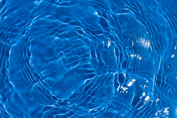 Blue water with ripples on the surface. Defocus blurred transparent blue colored clear calm water surface texture with splashes and bubbles. Water waves with shining pattern texture background.
