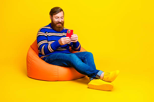 istock Bearded man in striped sweater using a smartphone on vibrant yellow background 2235367927
