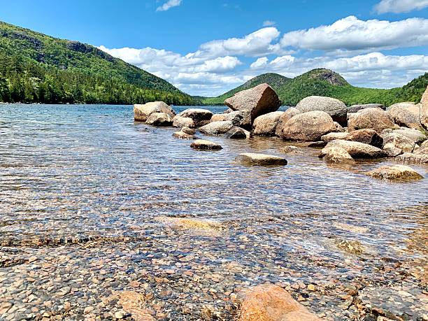 A tranquil blue lake nestled among vibrant green mountains, set beneath a bright sky dotted with scattered clouds. This serene natural landscape is ideal for outdoor adventure, hiking, and scenic travel destinations.