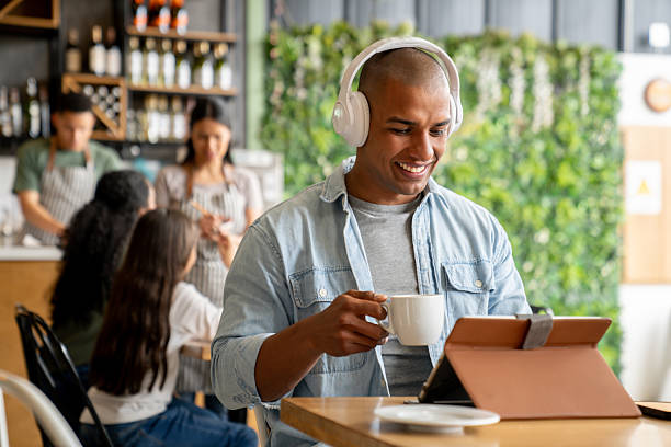 Happy Latin American man working at a cafe using his digital tablet and headphones - lifestyle concepts