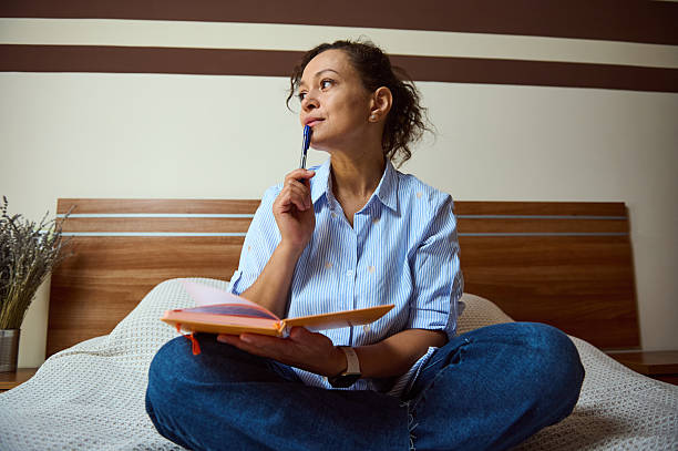 istock Thoughtful Woman Writing Notes in Journal While Sitting on Bed 2235396251