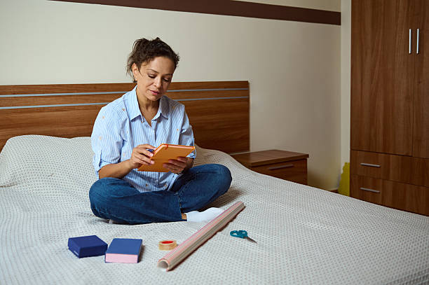 istock Woman Wrapping Gifts on a Bed While Using a Digital Tablet 2235396253