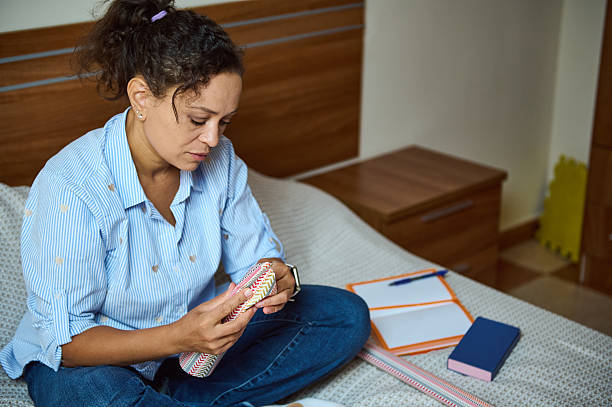 Woman Sitting on Bed Analyzing Items with Desk Materials Nearby