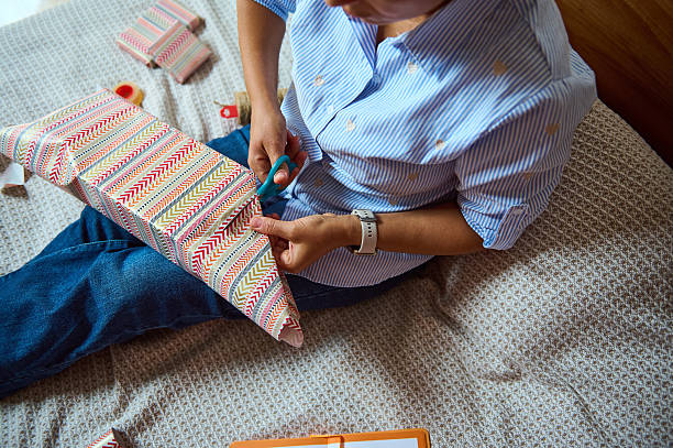 istock Person Wrapping Gift with Decorative Paper on a Cozy Bed Setting 2235396320