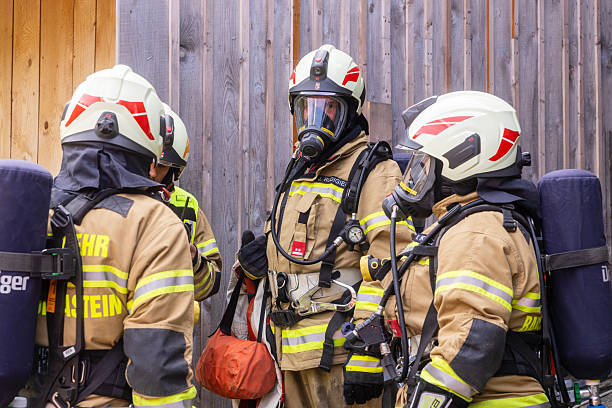 Austria, Salzburg State, Dorfgastein - September 13, 2025: Firefighters dressed in protective uniforms and helmets gather to discuss tactics before conducting a training drill in a suburban setting, surrounded by wooden structures.