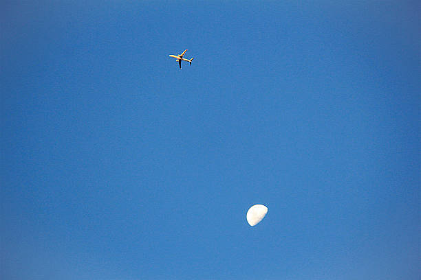 istock An airplane flies past the moon in a clear blue sky 2235429914