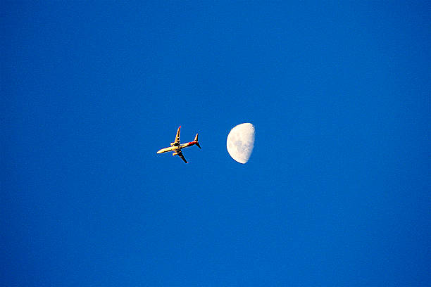 istock An airplane soaring across a clear blue sky with the moon in view 2235429983