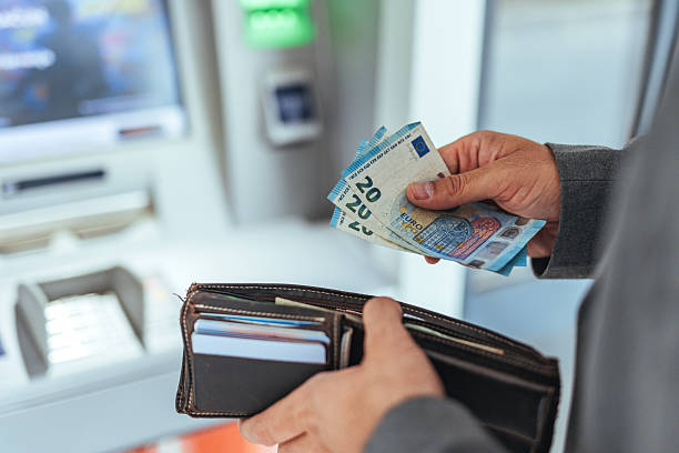 istock Individual Withdraws Cash at an ATM While Holding Wallet and Euro Notes 2235440113