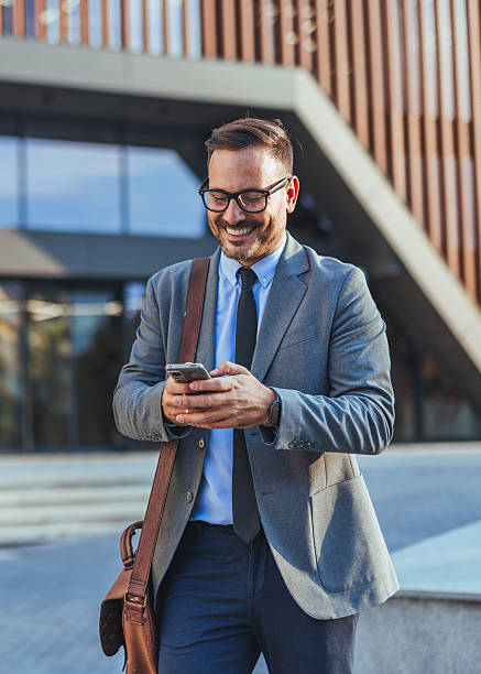 istock Smiling Businessman Using Smartphone Outside Modern Office Building 2235440117