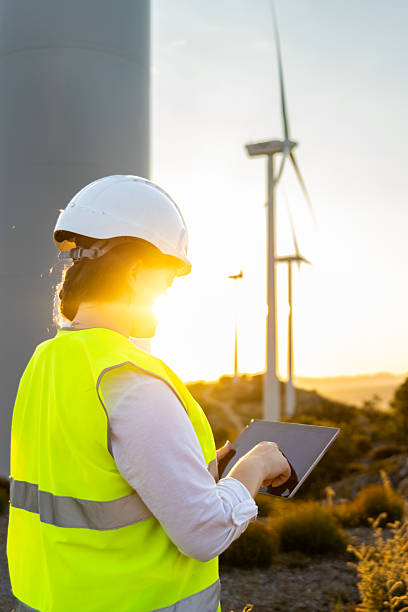 istock Female engineer working with digital tablet at wind turbine power plant during sunset 2235442131