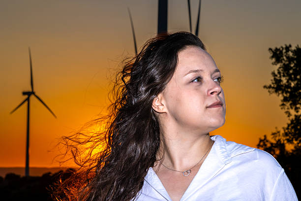 Young woman engineer looking at wind turbines at sunset, symbolizing renewable energy and ecological responsibility