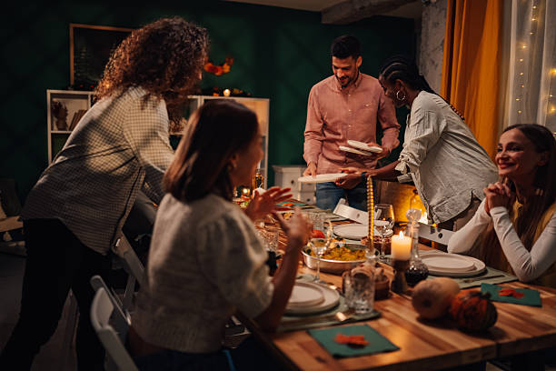 Friends bringing plates to thanksgiving dinner table