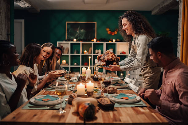 istock Young man bringing roasted turkey to thanksgiving table with friends 2235444191
