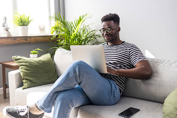 istock Man Relaxing on Couch Using Laptop at Home with a Bright Smile 2235444832