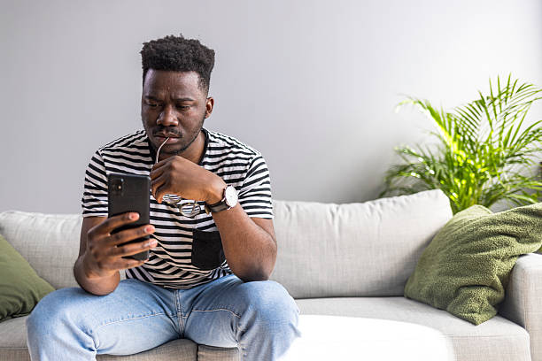 istock Man Relaxing on Couch Using Smartphone in Bright Living Room 2235444837
