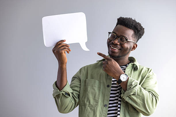 istock Smiling Man Holding a Blank Speech Bubble and Pointing to It 2235444873