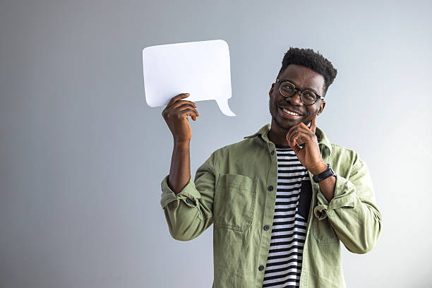 istock Smiling Man Holding Speech Bubble and Pondering Ideas Against Gray Background 2235444875