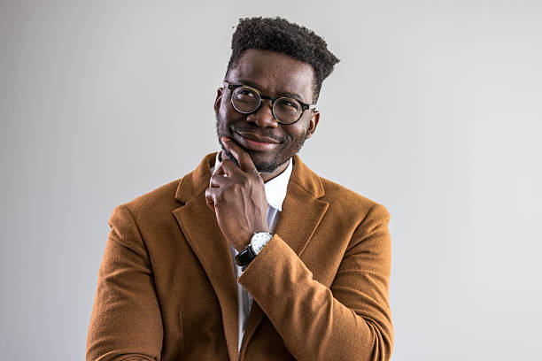 Man wearing glasses and a blazer, posing with a thoughtful expression and confident posture, isolated against a studio backdrop.