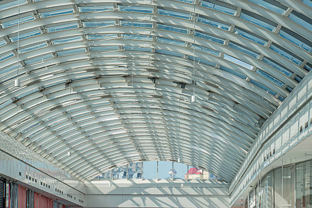 istock Modern architectural interior with curved, translucent ceiling and walls, natural light filtering, dappled shadows, central glass-enclosed walkwaybridge, dark floor contrast, soft reflections, open 2235447226