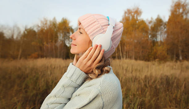 Inspired young woman enjoying listening to music in headphones outdoors in autumn forest stock photo