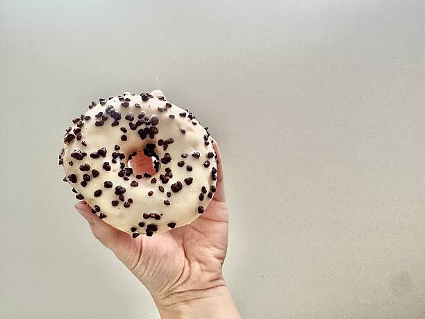 Hand holding donut with white icing and chocolate chips