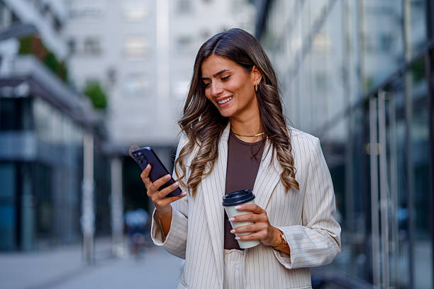 istock Smiling businesswoman walking through the city, using her smartphone while enjoying a coffee, exuding confidence and style 2235451875