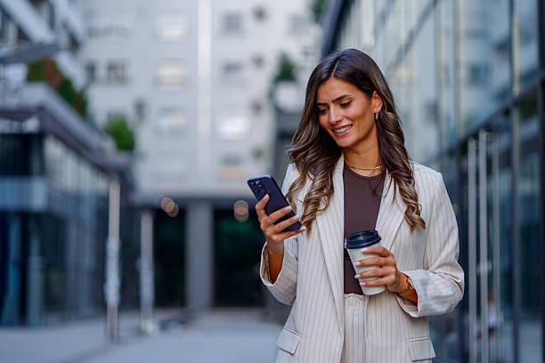 istock Young businesswoman walking through the city, using a smartphone while holding a coffee, exuding confidence and professionalism 2235451885