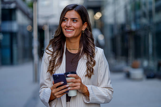 istock Professional woman walking outside, sipping coffee, checking smartphone with cheerful expression 2235452476