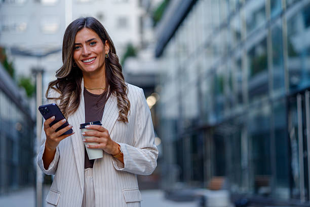 istock Professional woman texting, drinking takeout coffee near corporate headquarters 2235452512