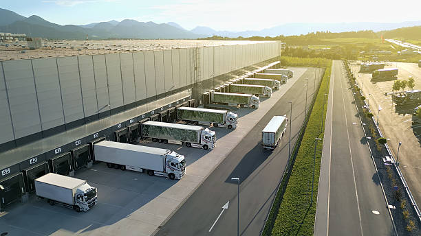 Aerial View Distribution Warehouse with Trucks at Loading Docks An aerial shot of aerial view of a bustling distribution warehouse with multiple trucks lined up at loading docks, set against a scenic mountain backdrop. The scene highlights efficient freight transportation and logistics operations, emphasizing modern infrastructure and cargo management. pick up truck stock pictures, royalty-free photos & images