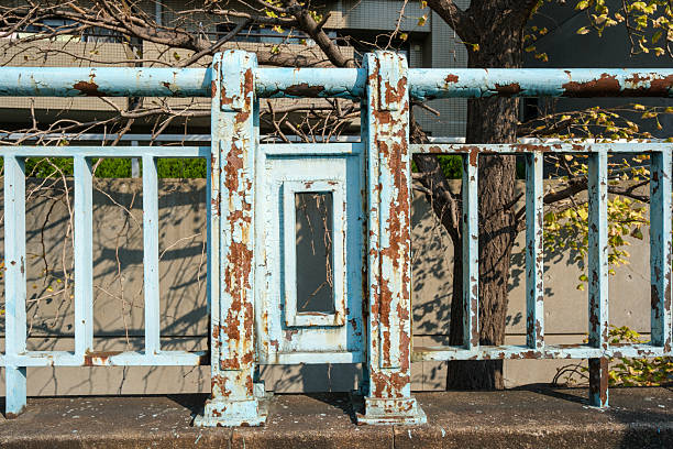Section of an old rusty light blue fence with peeling paint on a sunny day.