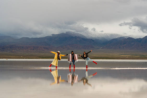 Three people in colorful outfits stand on reflective surface, moving forward with hope for future against big landscape of mountains. Their joyful expressions convey sense of adventure