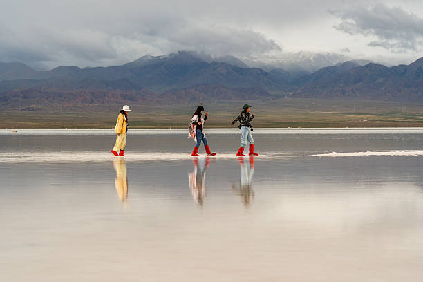 Exploring big landscape, three people are moving forward across reflective surface, embodying hope for future amidst stunning mountains and dramatic skies