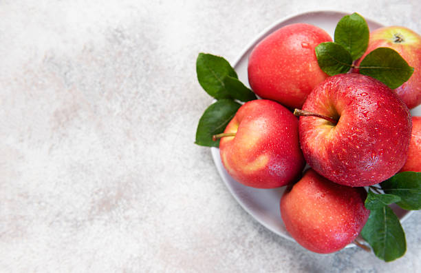 istock Fresh red apples with green leaves on white plate 2235486976