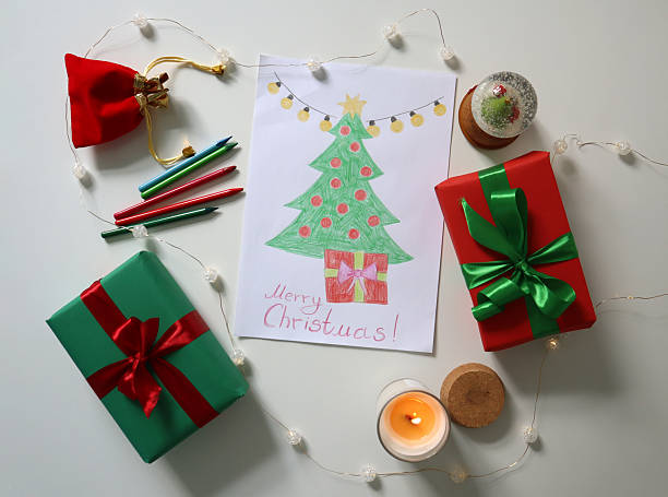 istock Child's drawing of decorated Christmas tree with gift underneath. Surrounded by wrapped Christmas decorations. 2235490838