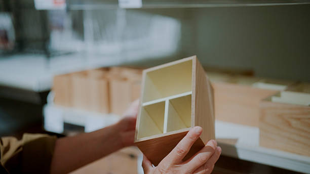 A close-up view of a man picking up and examining a wooden pencil box while browsing through home decor in a shopping mall.