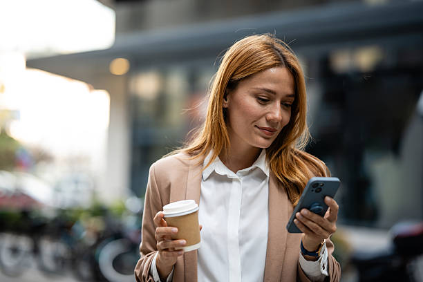 istock Businesswoman using smartphone and holding coffee outside office building 2235493948