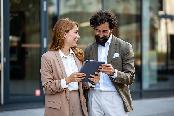 istock Business people using tablet and smiling outdoors near office building 2235493951
