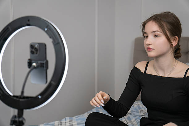 istock Young girl creating engaging video content in her cozy bedroom, using a smartphone and ring light to record a tutorial, embodying the modern influencer lifestyle 2235497619