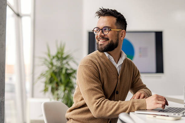 istock Bearded Professional In Brown Cardigan Working At Modern Office Desk With Natural Light 2235499481