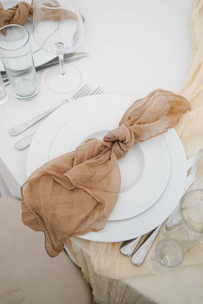White plate with brown napkin on wedding table next to glass tableware.