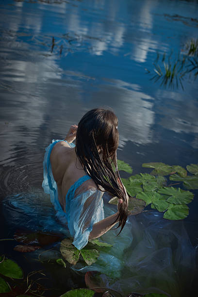 istock young woman sits gracefully in a calm lake, water gently lapping around her while she plays with her long hair. Bright blue dress contrasts beautifully with the surrounding greenery 2235500402