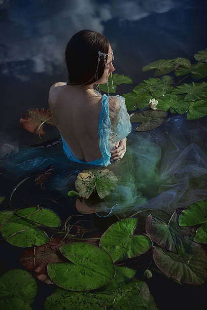 istock serene figure with flowing garments sits gracefully among lily pads in calm waters. reflection of clouds enhances the tranquil atmosphere at golden hour, creating a dreamlike setting 2235500408