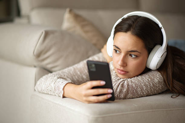 istock Pensive woman listening audio from headphone on a sofa 2235501312